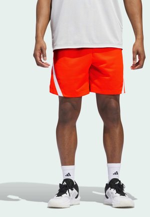 Felroze mesh sportshorts met een witte zijstreep, gecombineerd met zwart-witte sneakers en witte sokken met een logo.