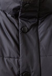 Czarna pikowana kurtka puchowa z wysokim kołnierzem i plastikowymi guzikami z przodu do zapinania. Gładka, błyszcząca faktura tkaniny.