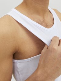 Débardeur en coton blanc à bretelles larges, design ajusté et texture douce. La main ajuste l'encolure.
