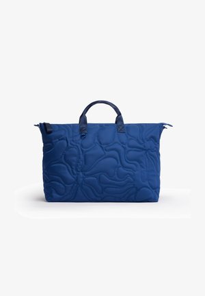 Borsa tote trapuntata blu con manici superiori e un sottile motivo astratto cucito su sfondo bianco.