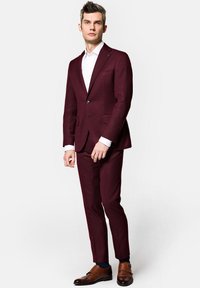 Bordowy garnitur o dopasowanym kroju, jednosuwakowa marynarka i spodnie z gładkim przodem. Biała koszula i brązowe skórzane buty dopełniają całości.