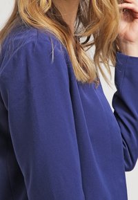 Granatowy top z długim rękawem o gładkiej fakturze. Dopasowany krój, z okrągłym dekoltem i prostym, czystym wzornictwem bez ozdób.