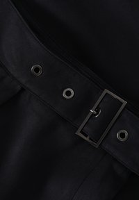 Cintura in tessuto nero con fibbia metallica e occhielli, caratterizzata da una superficie texturizzata e linee pulite, che enfatizzano un design elegante.