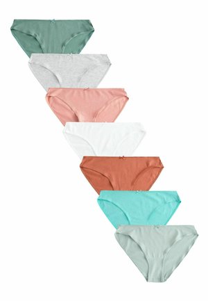 Gros plan d'une personne portant des sous-vêtements blancs en coton et un haut gris, montrant la hanche latérale et le bas du torse sur un fond clair uni.