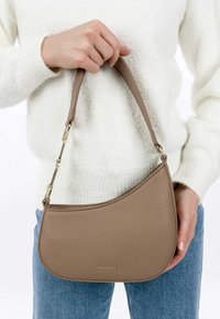 Sac à main en cuir tan avec un design incurvé, une courte sangle et des accents en métal doré. Tenue contre un fond clair.