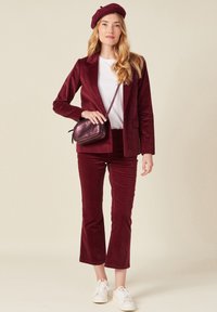 Bordeaux corduroy blazer, bijpassende broek en een wit T-shirt. Gecombineerd met een kleine metallic bordeaux tas en witte sneakers.