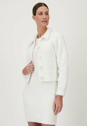 Witte, textuur-rijke, cropped jas met een kraag en sluiting met zes knopen, gedragen over een bijpassende jurk, die een samenhangend ontwerp laat zien.