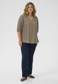 Top de manga corta con escote en V en color verde oliva con pequeños puntos de colores, combinado con jeans de pierna recta azul oscuro y bailarinas marrones.
