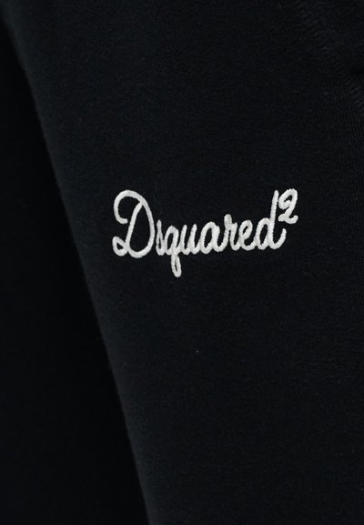 Μαύρο ύφασμα με λευκή κεντημένη κείμενο σε καλλιγραφική γραμματοσειρά που αναγράφει "Dsquared²" στο μανίκι.
