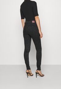 Svarta leopardmönstrade skinny jeans tillverkade av denim, med hög midja och en subtil lyster, kombinerade med svarta band sandaler.