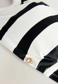 Tela a rayas blancas y negras con una textura suave, que presenta un botón circular dorado como detalle cerca de la costura.