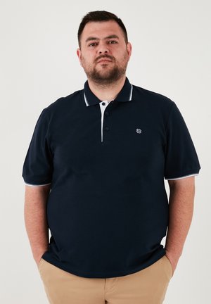 Jūras spēku polo krekls ar īsām piedurknēm, baltu apkakli un piedurkņu akcentiem, ar mazu izšūtu logotipu kreisajā krūtī.