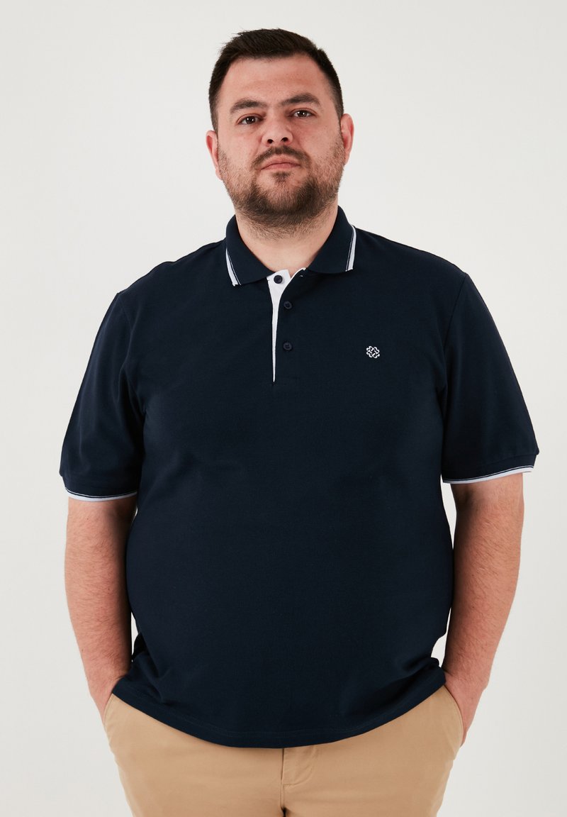 Námornícka polokošeľa s krátkymi rukávmi, bielym golierom a akcentmi na rukávoch, s malým vyšitým logom na ľavej hrudi.