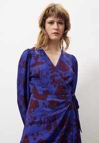 Wickelkleid aus blauer Stoff mit einem burgunderfarbenen Muster aus abstrakten Formen und Designs. Lange Ärmel und ein Bindeband in der Taille.