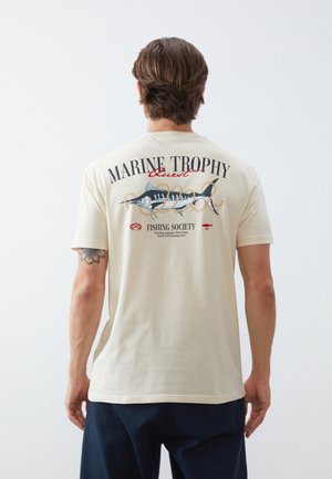 Katoenen t-shirt, crème kleur, met een groot grafisch ontwerp van een vis en tekst op de achterkant. Korte mouwen, casual pasvorm, voorkant zonder opdruk.