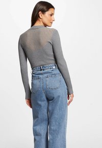 Graues, geripptes Langarmoberteil mit einem transparenten, gestreiften Rücken, kombiniert mit hochgeschnittenen, hellblauen Jeans. Auffälliges Rückendetail und Struktur.