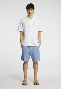 Bílé krátké tričko s límečkem, doplněné o světle modré šortky. Model má na sobě hnědé sandály. Materiál vypadá lehce a neformálně.