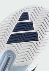 Semelle de chaussure blanche présentant un motif chevron texturé, des accents bleus et trois superpositions distinctes en caoutchouc marine disposées en forme triangulaire.