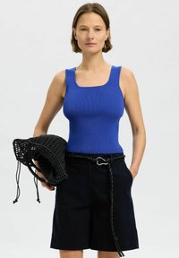 Niebieska rypsowa bluzka na ramiączkach z kwadratowym dekoltem, w połączeniu z czarnymi szortami i teksturowaną czarną siatkową torbą. Prosty i nowoczesny design.