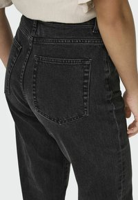 Kõrge vöökohaga mustad denim teksad sileda tekstuuriga, tagaküljel on tasku ja kerge tuhmumine, mis annab kaasaegse ilme.