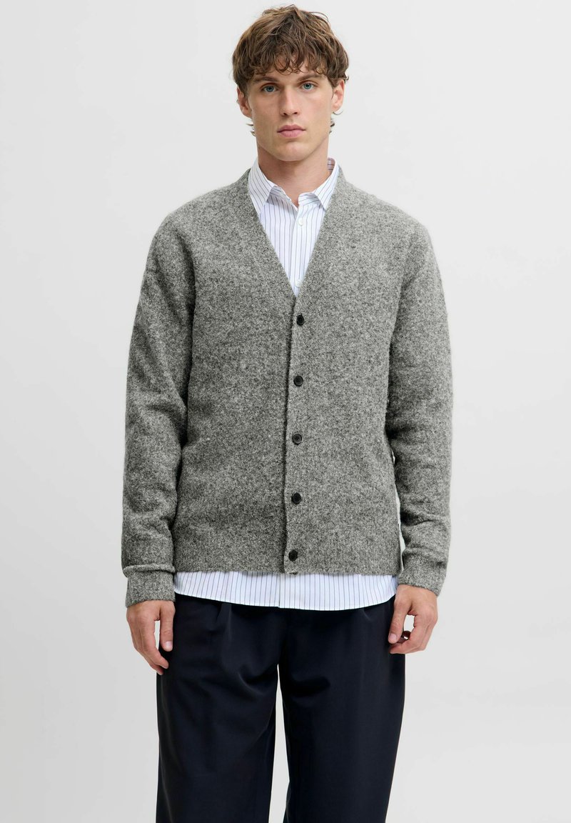 Grau gestrickte Wolle Cardigan mit V-Ausschnitt, Knopfschluss und gerippten Bündchen. Über einem weißen und blauen gestreiften Hemd getragen. Locker sitzendes Design.