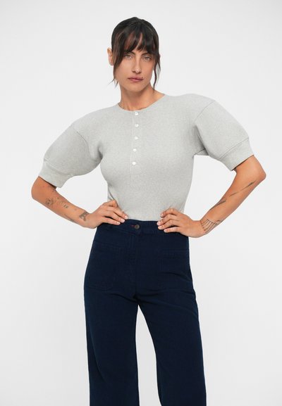 Top gri cu dungi, cu mânecă scurtă, guler rotund și deschidere cu nasturi, asociat cu pantaloni cu talie înaltă, de culoare albastru închis, cu croi larg.