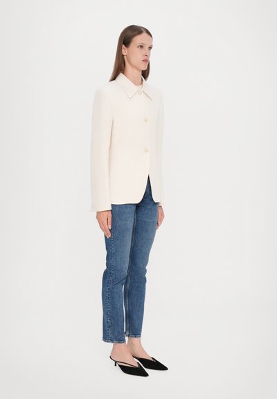 Cream-colored blazer with a pointed collar and two buttons, paired with blue skinny jeans and black pointed-toe heels.