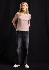 Hellrosa Langarmshirt mit Rundhalsausschnitt, kombiniert mit dunkelgrauen weit geschnittenen Jeans und weißen Sneakers. Einfaches Design, weiche Textur.