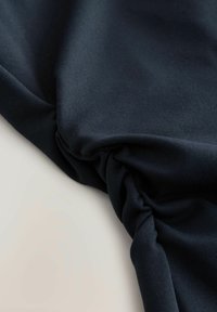 Jūras spēku zila auduma ar gludu tekstūru, kurā ir izgriezums, kur audums sakrājas, radot smalku drapēšanas efektu.