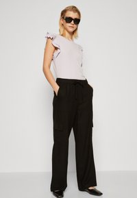 Top lavande avec des manches volantées, associé à un pantalon cargo noir à jambes larges avec poches. Des ballerines noires pointues complètent l'ensemble.