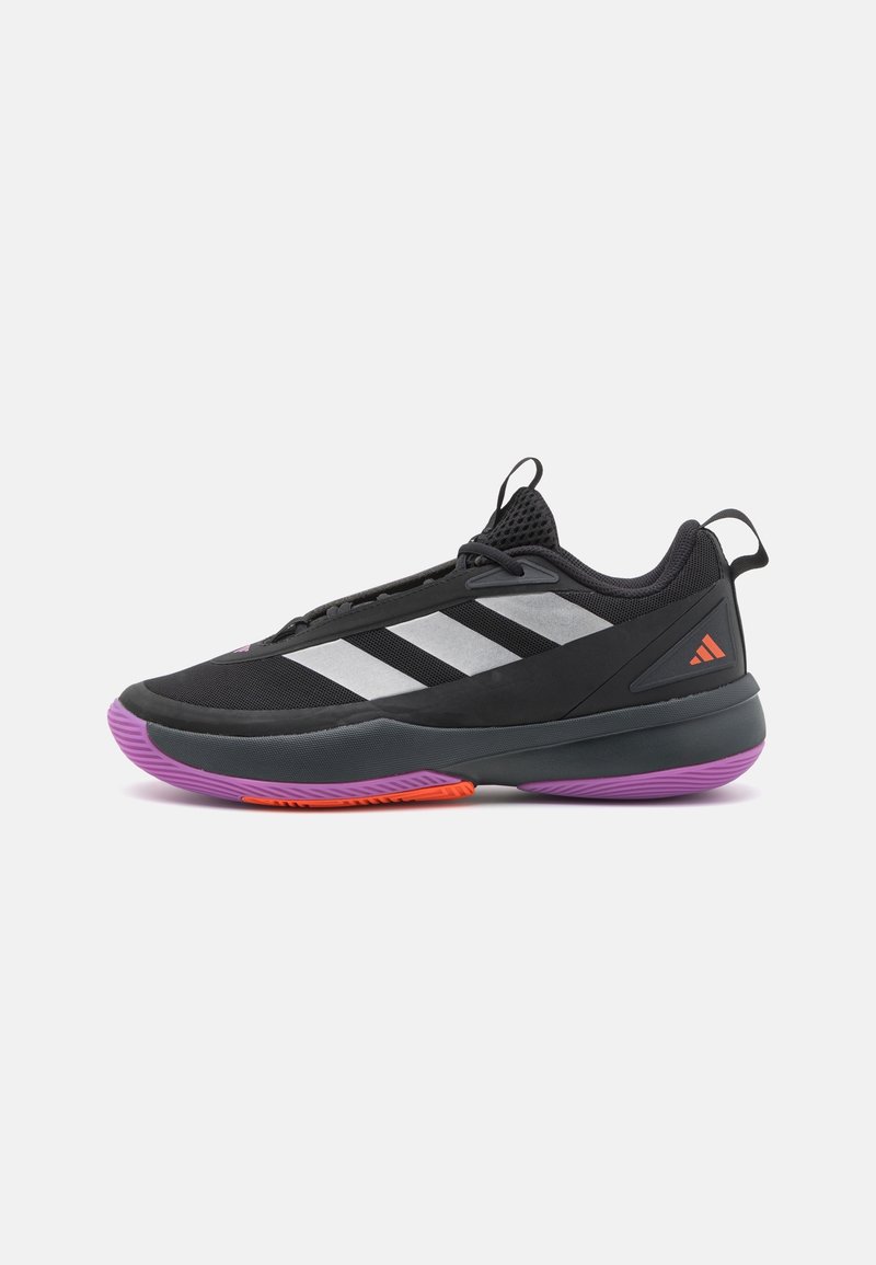 Chaussure de sport noire avec des bandes grises, des accents violets et orange sur la semelle, et des languettes sur la languette et le talon, vue de profil.