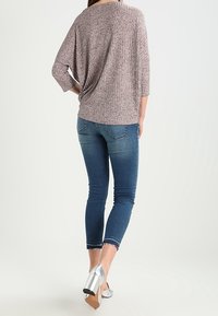 Suéter ligero y texturizado en color rosa, con mangas tres cuartos; combinado con jeans de denim azul ajustados y zapatos de tacón alto plateados.
