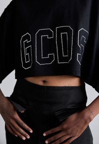 Camiseta corta negra con grandes letras "GCDS" adornadas con strass blancos, combinada con pantalones negros de cintura alta con bolsillos laterales.