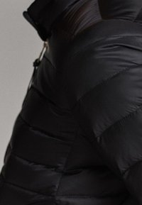 Veste matelassée noire avec un motif en losanges et une finition brillante. Comprend une fermeture éclair et des éléments de design minimalistes.