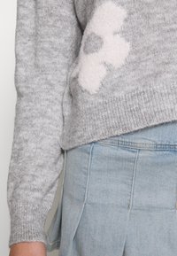 Maglione grigio a maglia con un motivo floreale rosa chiaro e soffice sulla parte anteriore, abbinato a pantaloni di denim blu chiaro.