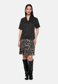 Schwarzes Kurzarm-Top mit einem Bindedetail, kombiniert mit einem plissierten Rock mit Leopardenmuster und vertikalen schwarzen Streifen. Schwarze kniehohe Stiefel.