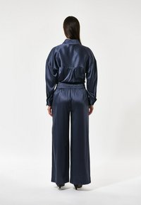 Completo in satin blu navy composto da una camicia dal taglio rilassato con colletto e pantaloni a gamba larga con vita elastica, entrambi caratterizzati da una texture liscia.