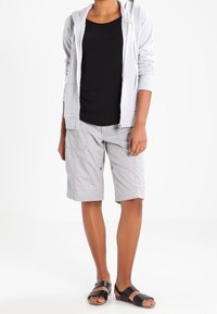 Ljusgrå shorts med cargofickor, matchade med en svart tanktop och en ljusgrå zip-up hoodie. Svarta sandaler fulländar outfiten.
