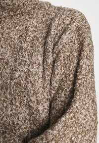 Maglione marrone con texture, caratterizzato da un motivo di maglia morbido e peloso. Presenta una vestibilità ampia e un colletto ripiegato. Vista ravvicinata della superficie del tessuto.