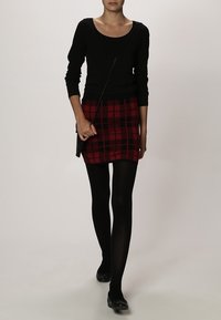 Un haut noir à manches longues associé à une mini-jupe ajustée en tartan rouge et des collants noirs, complété par des ballerines noires et un petit sac à bandoulière.