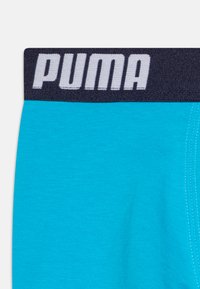 Muške bokserice u svijetloplavo tirkiznoj tkanini s mekom teksturom i tamnoplavim elastičnim pojasom na kojem je bijeli "PUMA" logo.