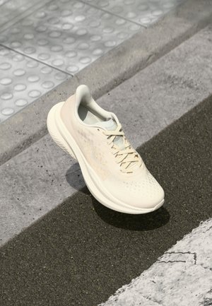 Jasnobeżowy but sportowy z sznurowadłami spoczywający na teksturowanym chodniku i krawężniku z betonu, ukazany pod kątem, aby pokazać widok z boku i z góry.
