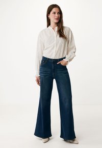 Wijdvallende donkerblauwe jeans met een hoge taille en een gladde textuur, gecombineerd met een witte blouse met knopen die bloemapplicaties heeft.