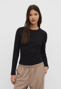 Sort langærmet T-shirt med rund hals, glat tekstur, tætsiddende design, parret med beige trækbånds bukser.