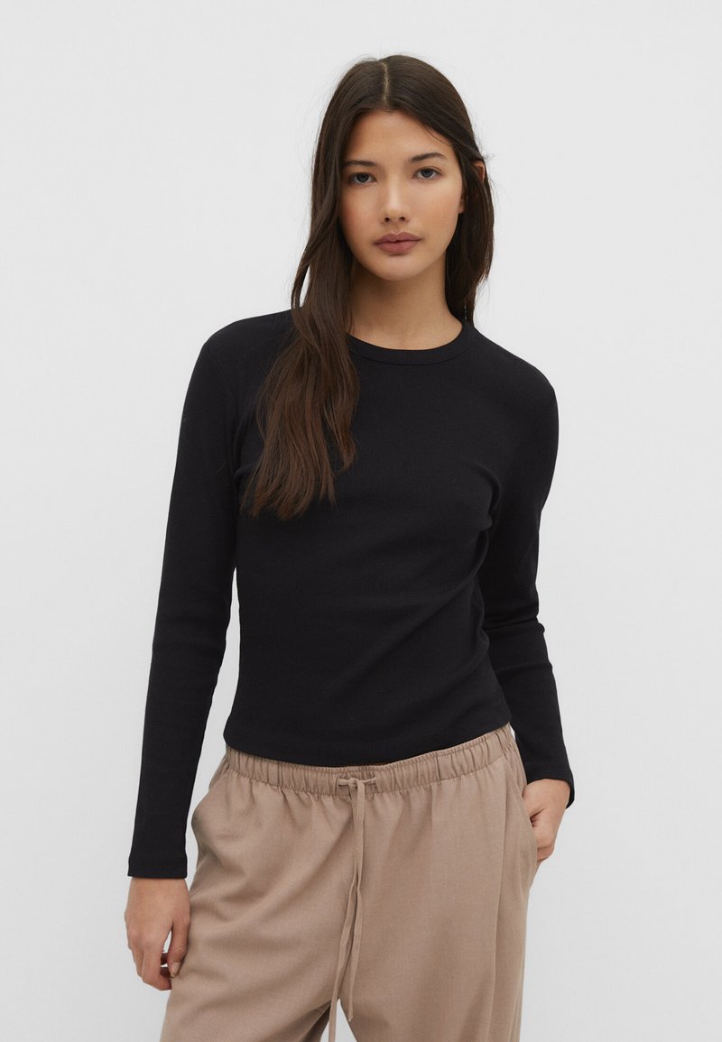 Sort langærmet T-shirt med rund hals, glat tekstur, tætsiddende design, parret med beige trækbånds bukser.