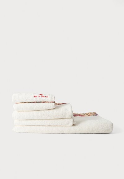 Pile de serviettes blanches pliées aux bords décorés, une serviette avec un logo rouge brodé sur un fond clair uni.