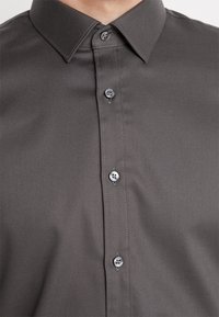 Szara koszula zapinana na guziki, wykonana z teksturowanej tkaniny, z klasycznym kołnierzykiem, sześcioma guzikami i czystym, dopasowanym krojem.