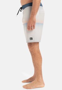 Helle graue Boardshorts mit dunkelblauem Bund, horizontalen blauen und orangefarbenen Streifen sowie einem schwarzen Logopatch nahe dem Saum. Entworfen für Strandbekleidung.