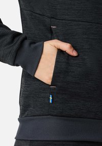 Dark gray sweatshirt featuring a side pocket, textured fabric, ribbed cuffs, and a small blue-and-yellow flag emblem.