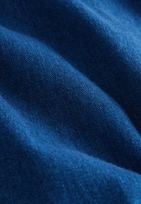 Primo piano di tessuto blu piegato che mostra una trama tessuta dettagliata e pieghe morbide.
